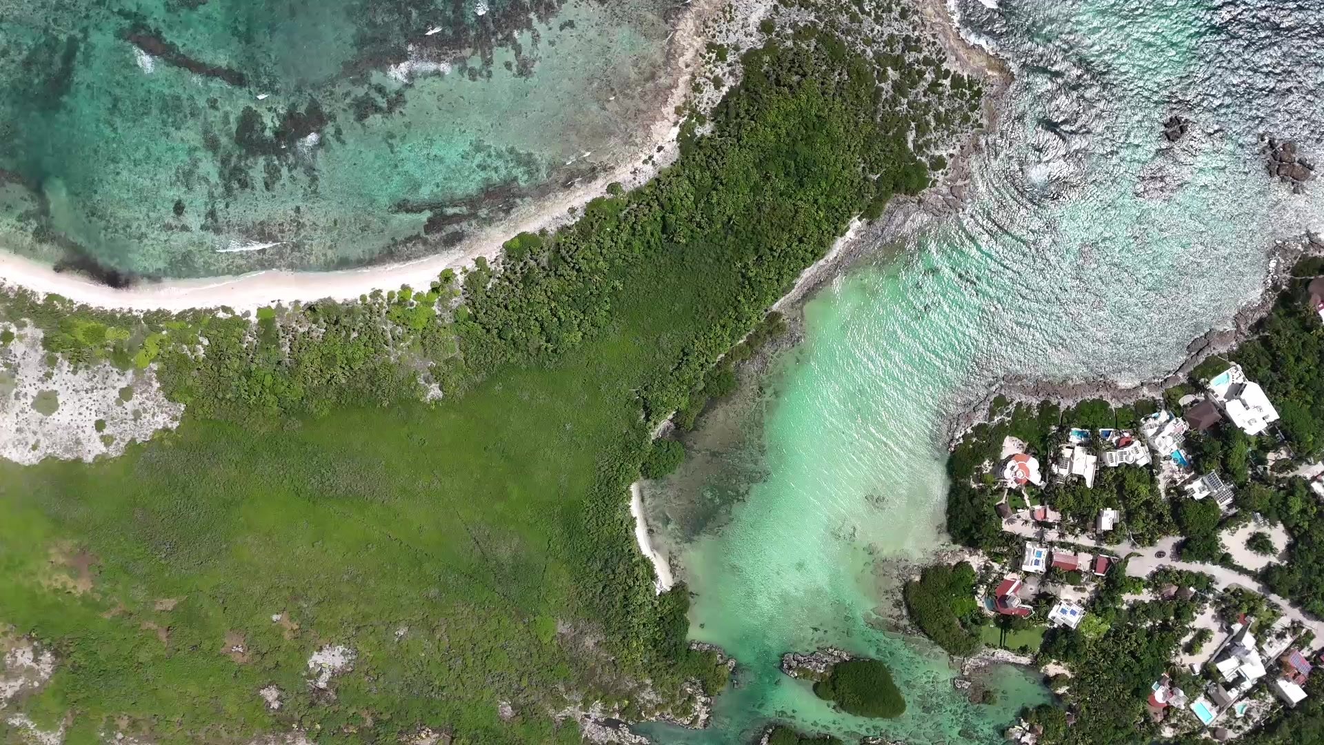 Aerial view of a turquoise lagoon opening to the sea, with jungle and low-rise homes beside it